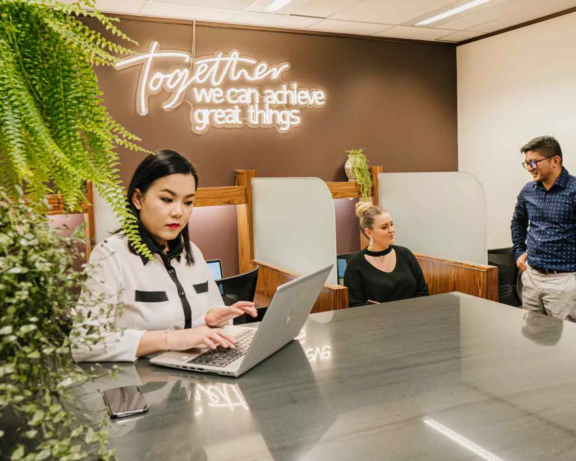 Close up on a client working in a modern coworking shared space on a long table surrounding booths in Servcorp 91 King William Street, Adelaide